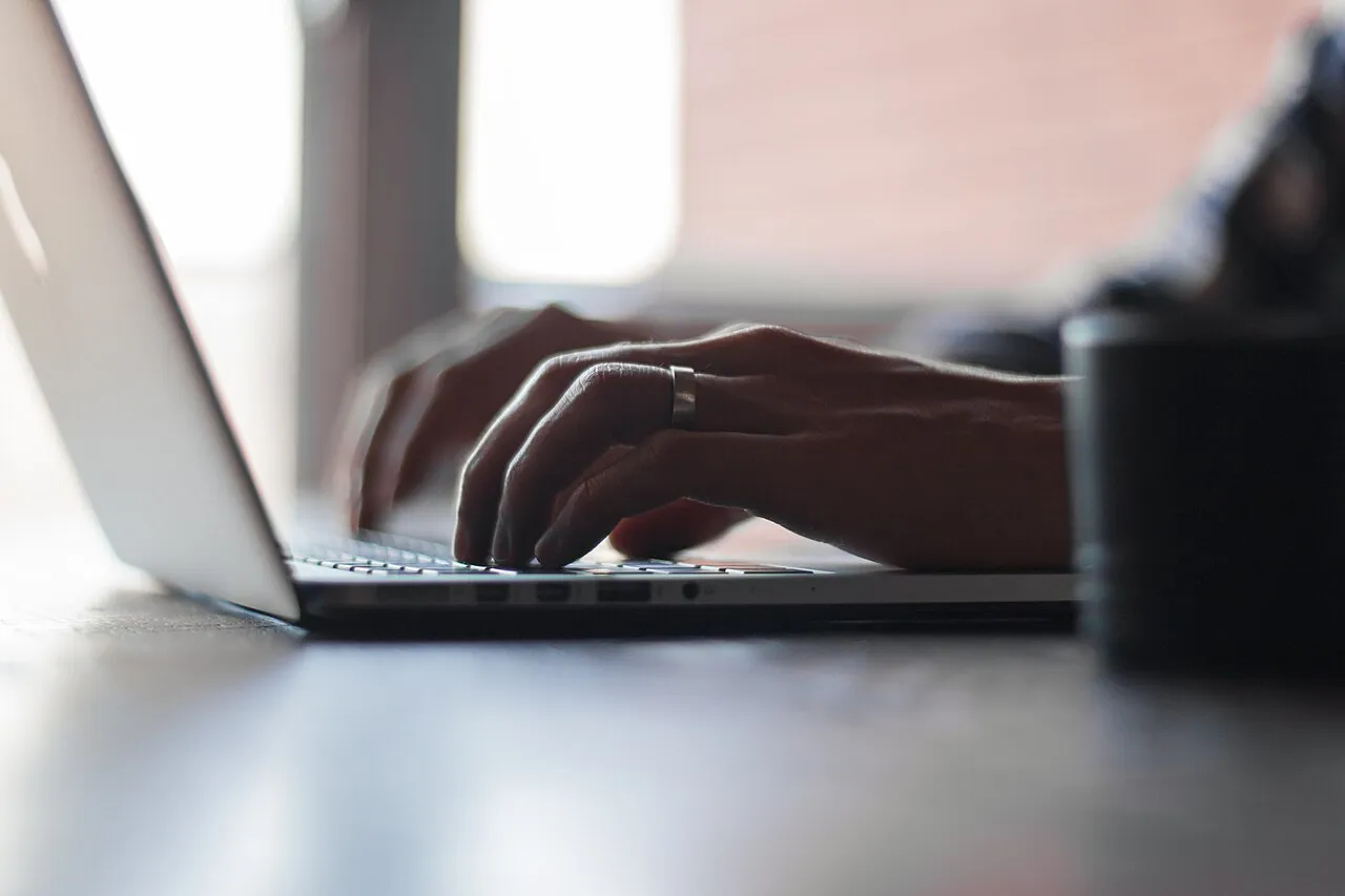 Hands typing on a laptop at a work desk