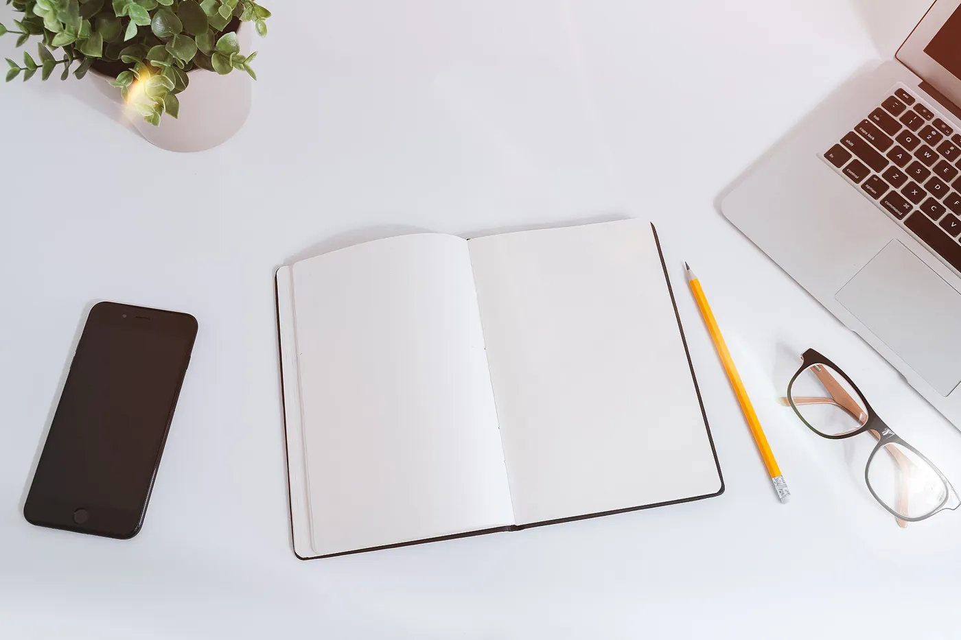 A notebook, laptop and phone on a work desk